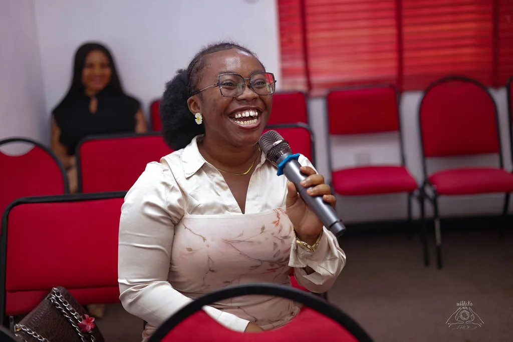 A woman laughing as she speaks into a microphone from her seat in the audience