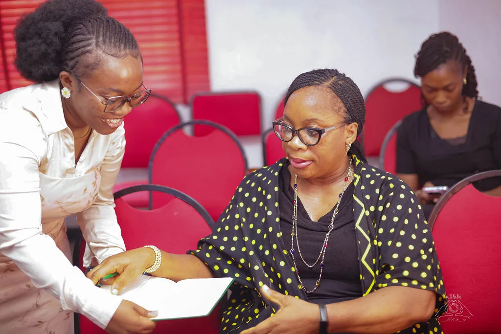 One woman leaning in to talk another through the notes in her hand