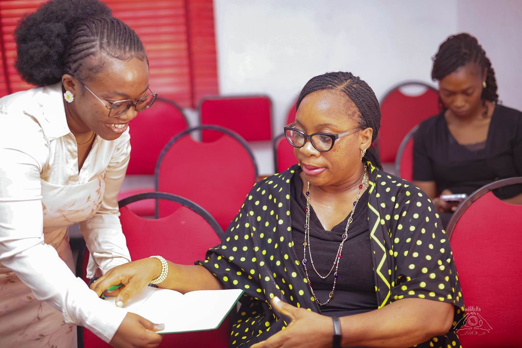 Two women seated together, one talking the other through her notes