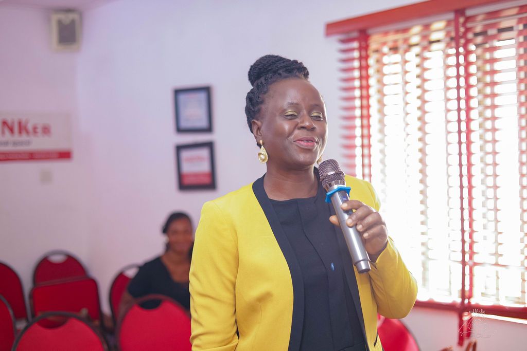 A woman in a yellow blazer speaking into a microphone